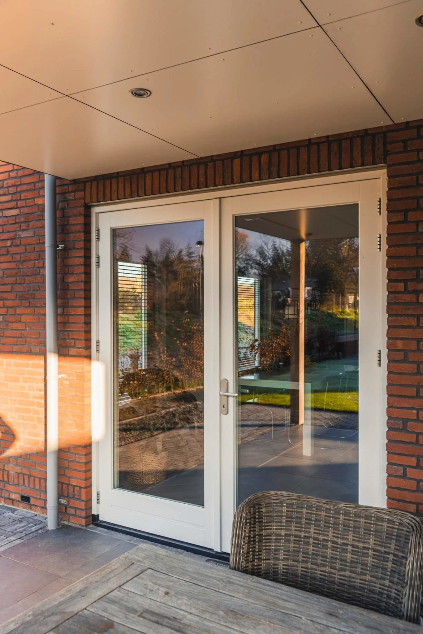 Dubbele houten buitendeur met glasvlakken en aluminium deurkrukken, geplaatst onder een overkapping tegen een gevel van rood metselwerk – Toelevering Online