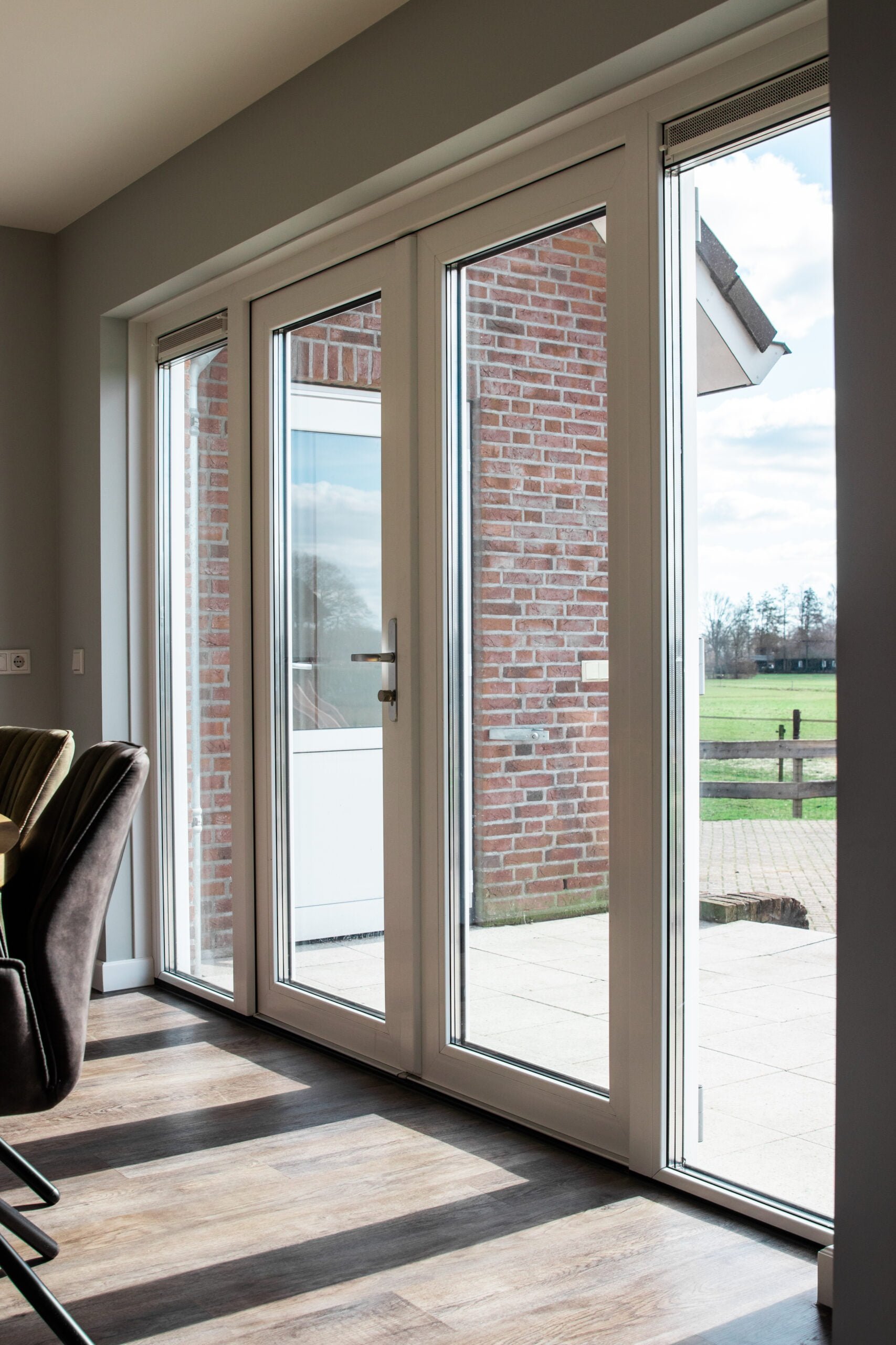 Witte dubbele tuindeuren met zijlichten in kunststof kozijn, met uitzicht op terras en weiland – Toelevering Online